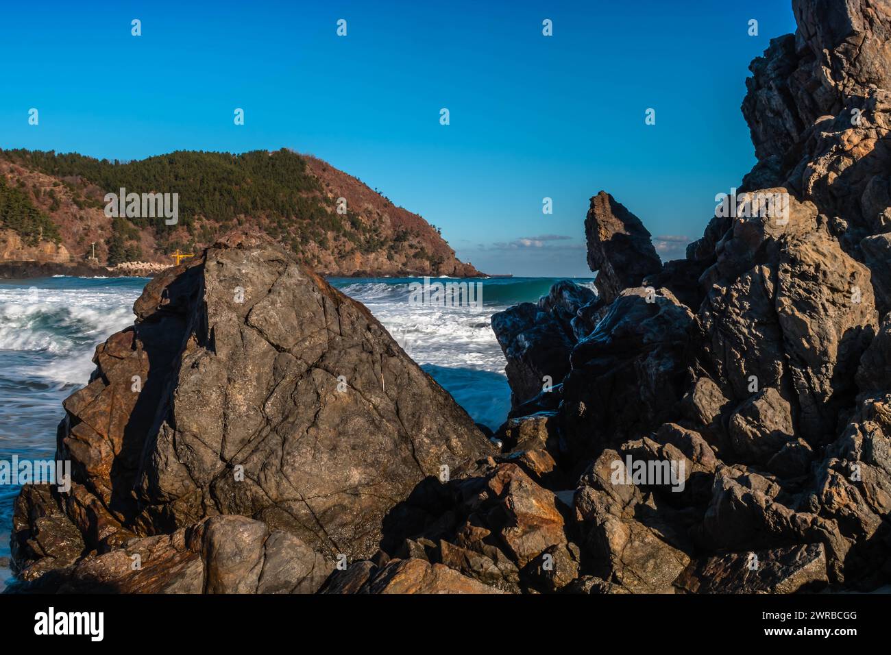 Les vagues de mousse de l'océan embrassent le paysage rocheux sous le ciel bleu expansif, en Corée du Sud Banque D'Images