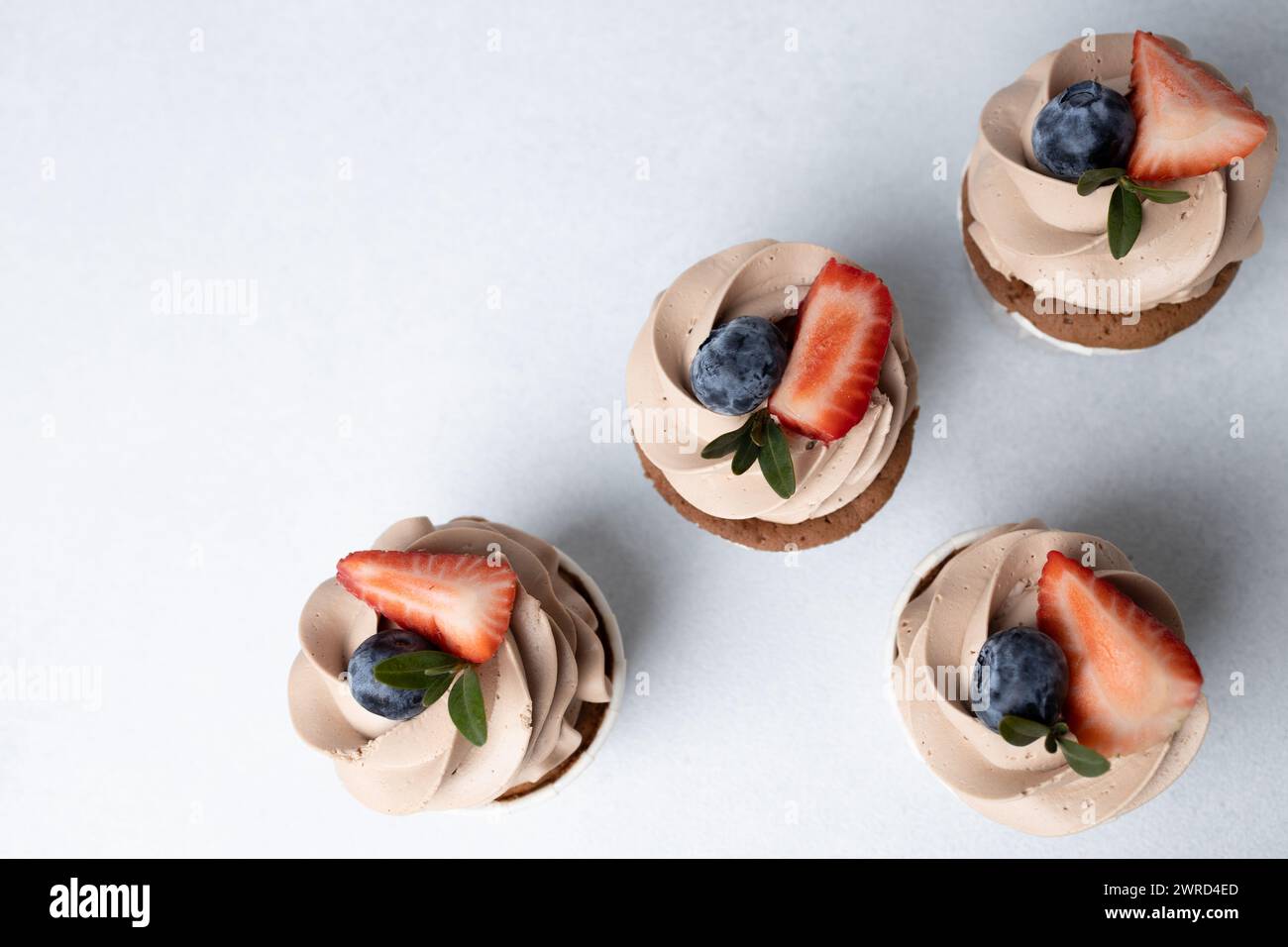Vue de dessus de cupcakes au chocolat avec glaçage au fromage à la crème, fraise et myrtille sur fond clair Banque D'Images