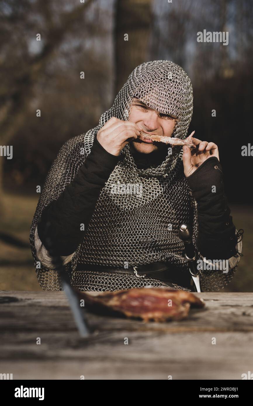 Homme armé d'infanterie médiévale assis près de la table en bois Banque D'Images
