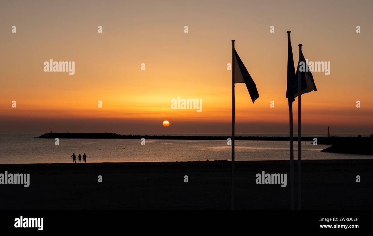 Les gens sur la plage regardant le coucher du soleil sur la mer du Nord et South Pier du port de Hvide Sande, Jutland central, Danemark Banque D'Images