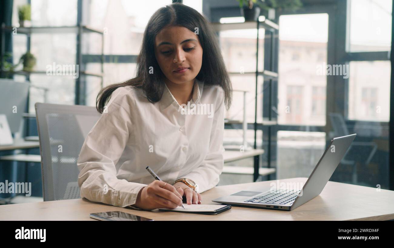 Étudiante multiraciale étudiant en ligne sérieuse femme d'affaires occupée dans le bureau écrivant des notes des idées de tâches d'affaires dans le cahier de travail avec un ordinateur portable Banque D'Images
