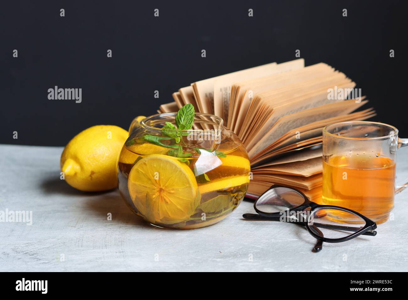 Théière en verre avec thé au gingembre et au citron, livre ouvert et verres de lecture sur une table. La nature morte du jour d'hiver. Concept d'alimentation saine. Banque D'Images