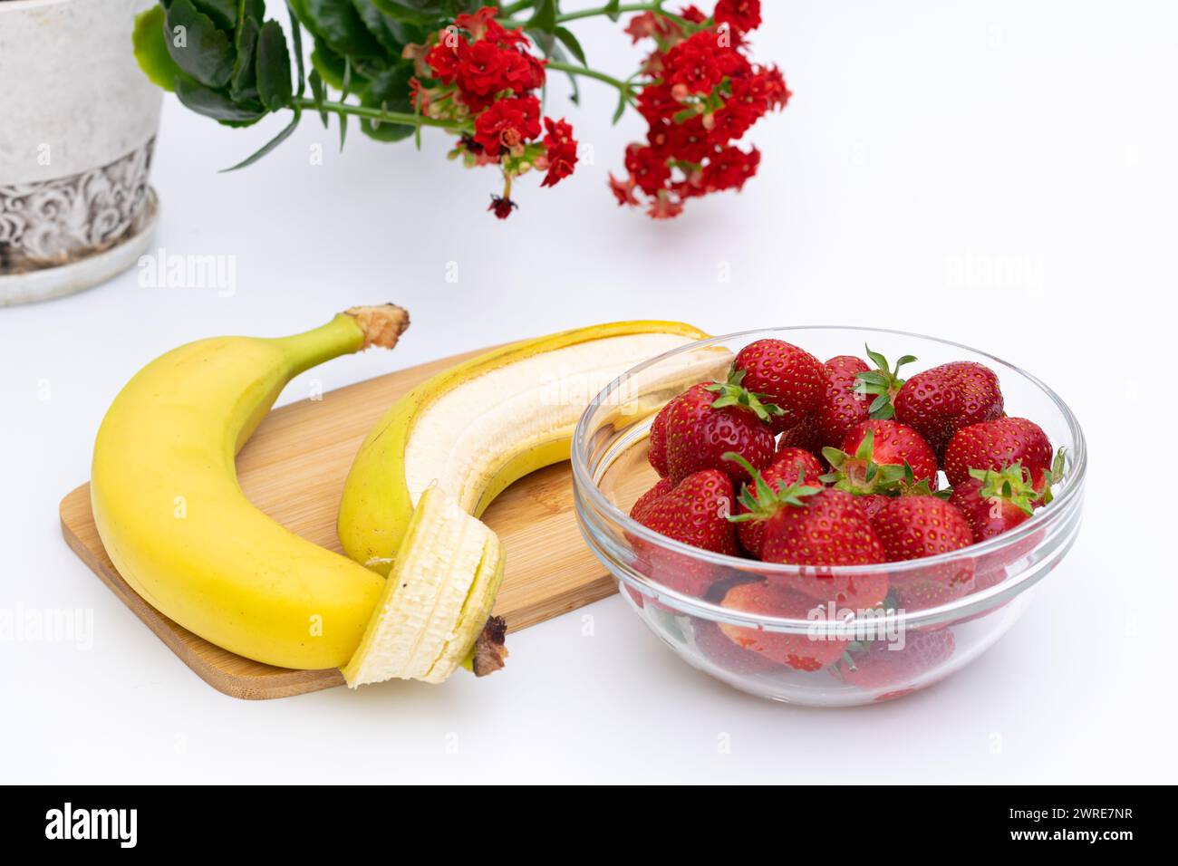 Bananes de fruits et fraises dans un bol en verre avec fleur rouge sur fond, concept de consommation de fruits frais Banque D'Images