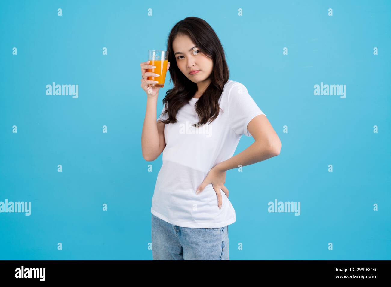 Belle femme buvant de l'orange dans un verre elle portait une chemise blanche, souriant, et ses yeux étaient brillants. dans le fond bleu Banque D'Images