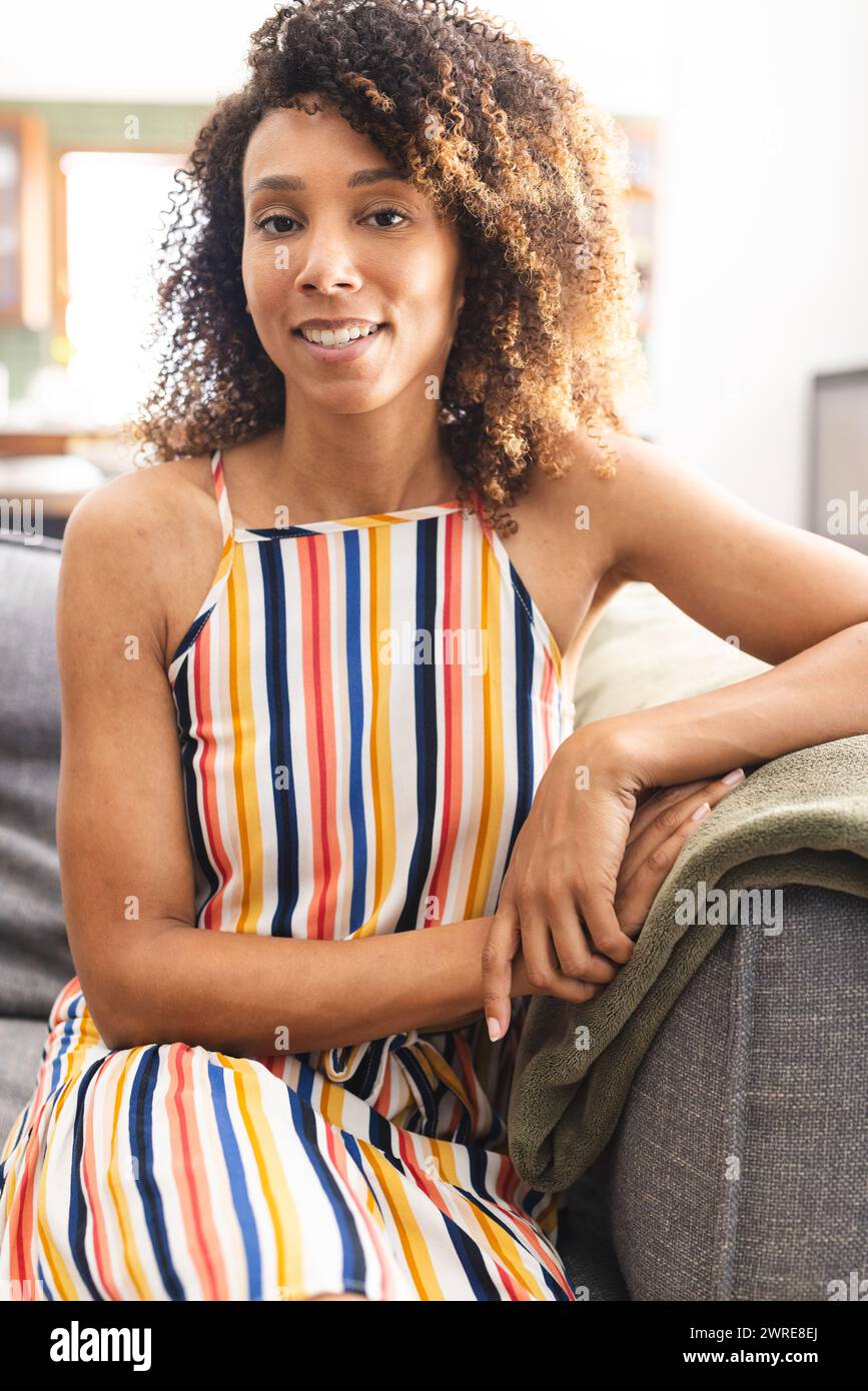 Femme biraciale avec les cheveux bruns bouclés porte une robe rayée colorée Banque D'Images