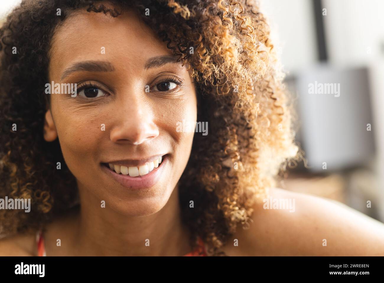 Une femme biraciale aux cheveux bouclés sourit chaleureusement à la caméra Banque D'Images