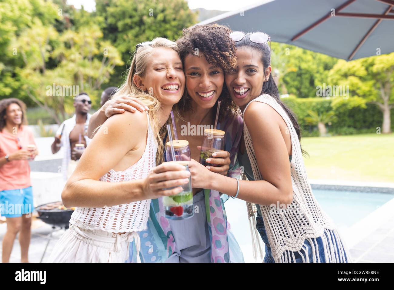 Trois amies féminines diverses embrassent et sourient à une fête de piscine extérieure Banque D'Images