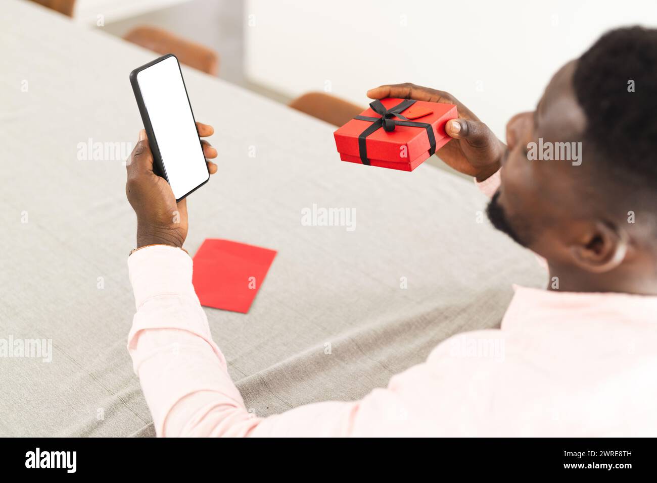 Homme afro-américain tient un téléphone avec un écran blanc et une petite boîte cadeau rouge avec espace de copie Banque D'Images