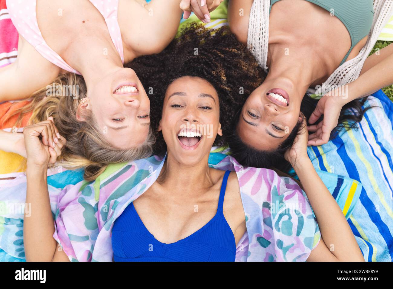 Trois femmes sont allongées sur une couverture colorée, les têtes ensemble, souriant joyeusement Banque D'Images