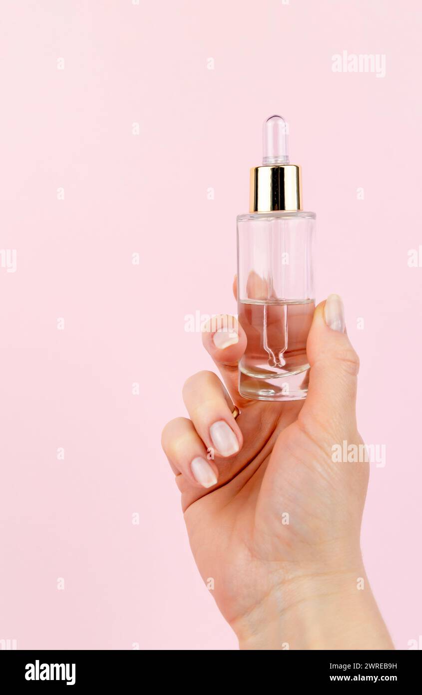 Pot en verre avec sérum à la main sur fond rose pastel. Le concept de soin du visage et de lissage des rides. Banque D'Images