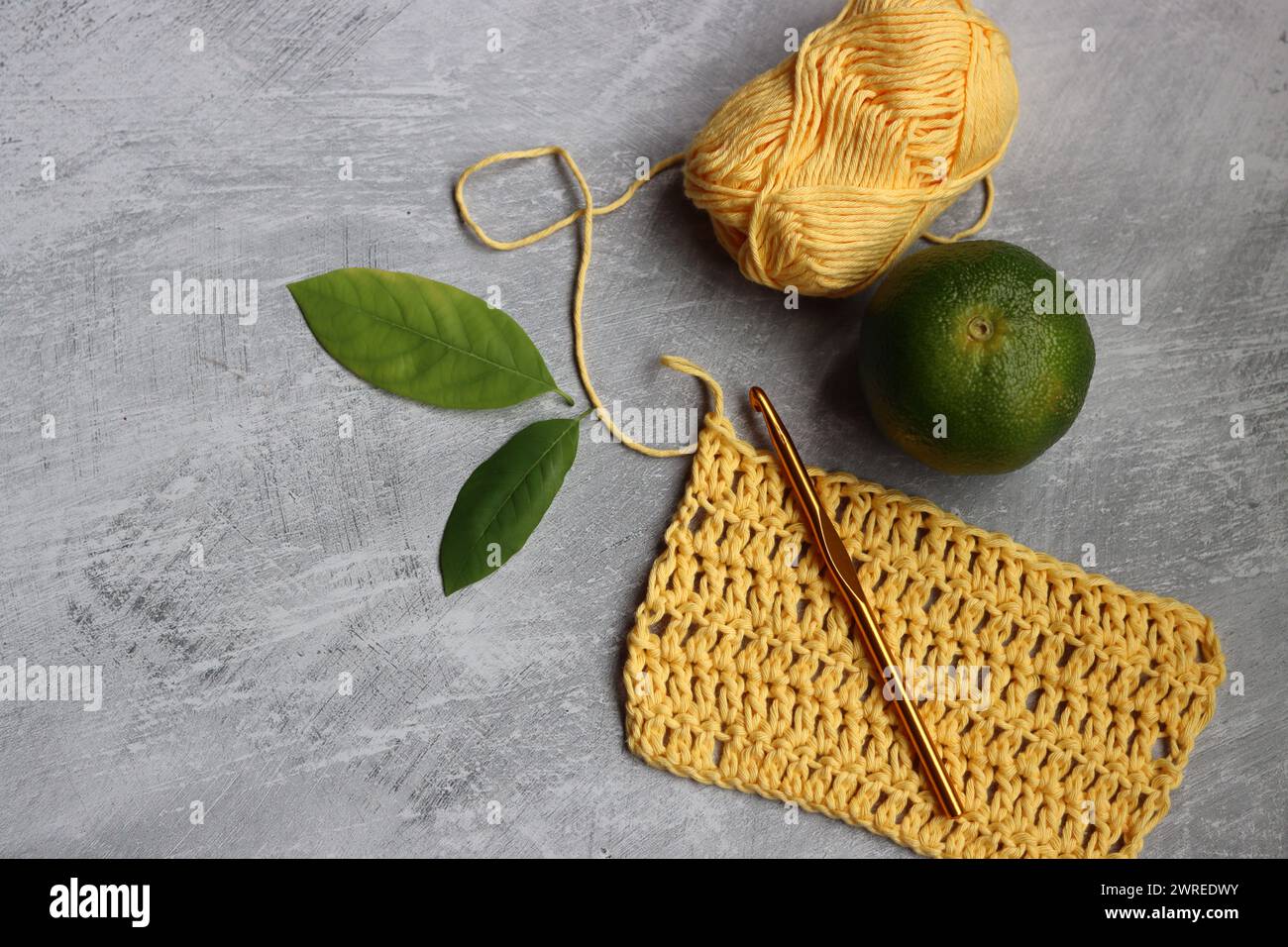 Crochet écharpe en cours. Crochet crochet, fil de coton jaune, citron vert et feuilles sur fond gris, vue de dessus Banque D'Images