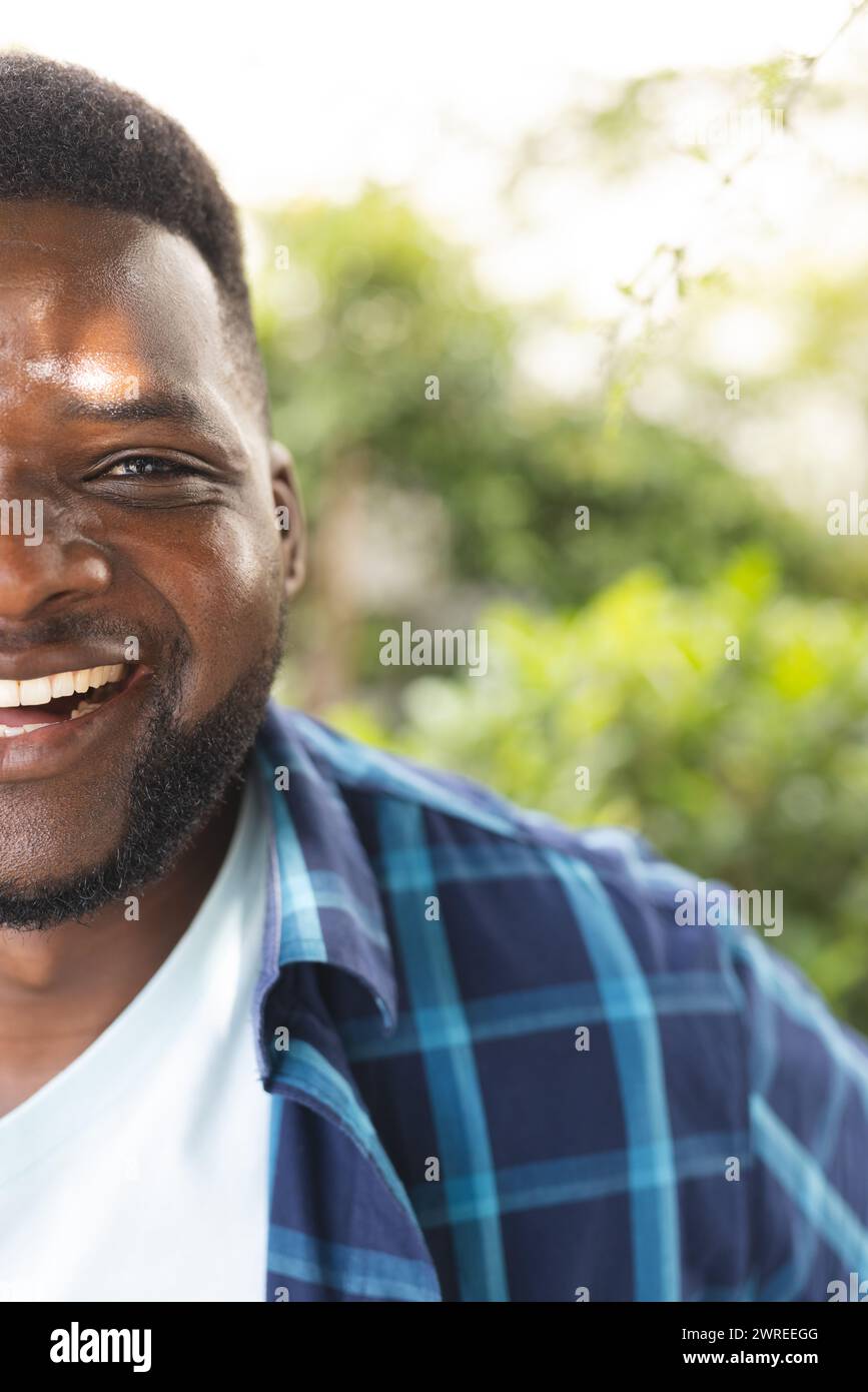 Homme afro-américain avec un sourire rayonnant, portant une chemise à carreaux bleue, avec espace copie, dans un jardin Banque D'Images