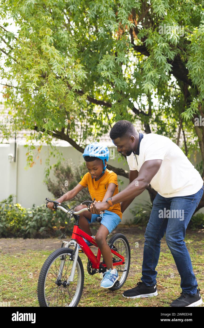 Père afro-américain apprend à son fils à faire du vélo dans un jardin luxuriant Banque D'Images