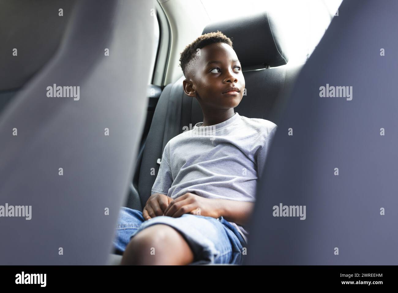 Garçon afro-américain assis dans une voiture, regardant par la fenêtre réfléchie Banque D'Images