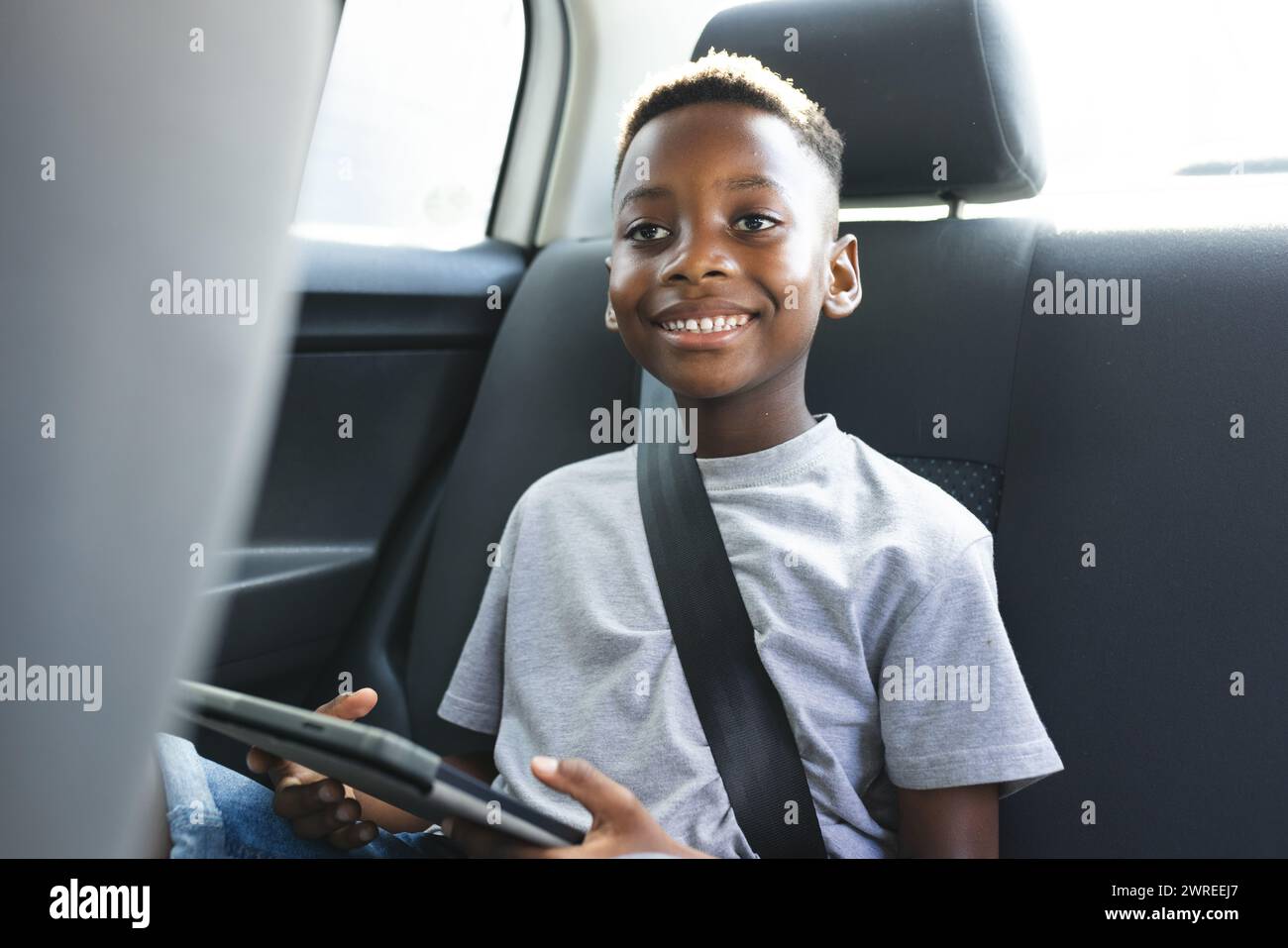 Garçon afro-américain avec une tablette sourit en étant assis dans une voiture Banque D'Images