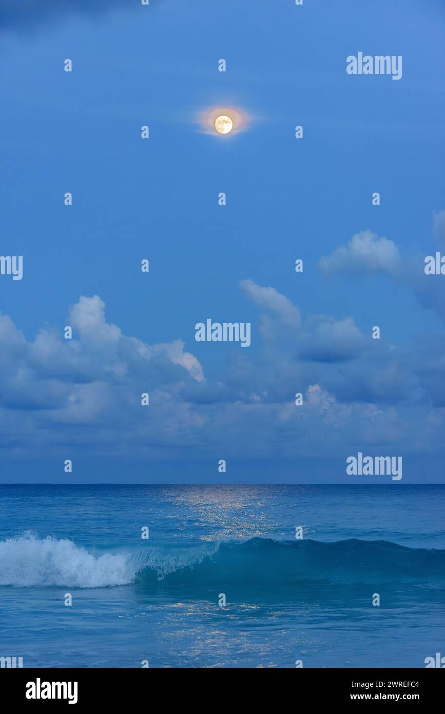 Moisson Lune illuminant les nuages et se reflétant dans la mer avec des vagues brisantes Banque D'Images