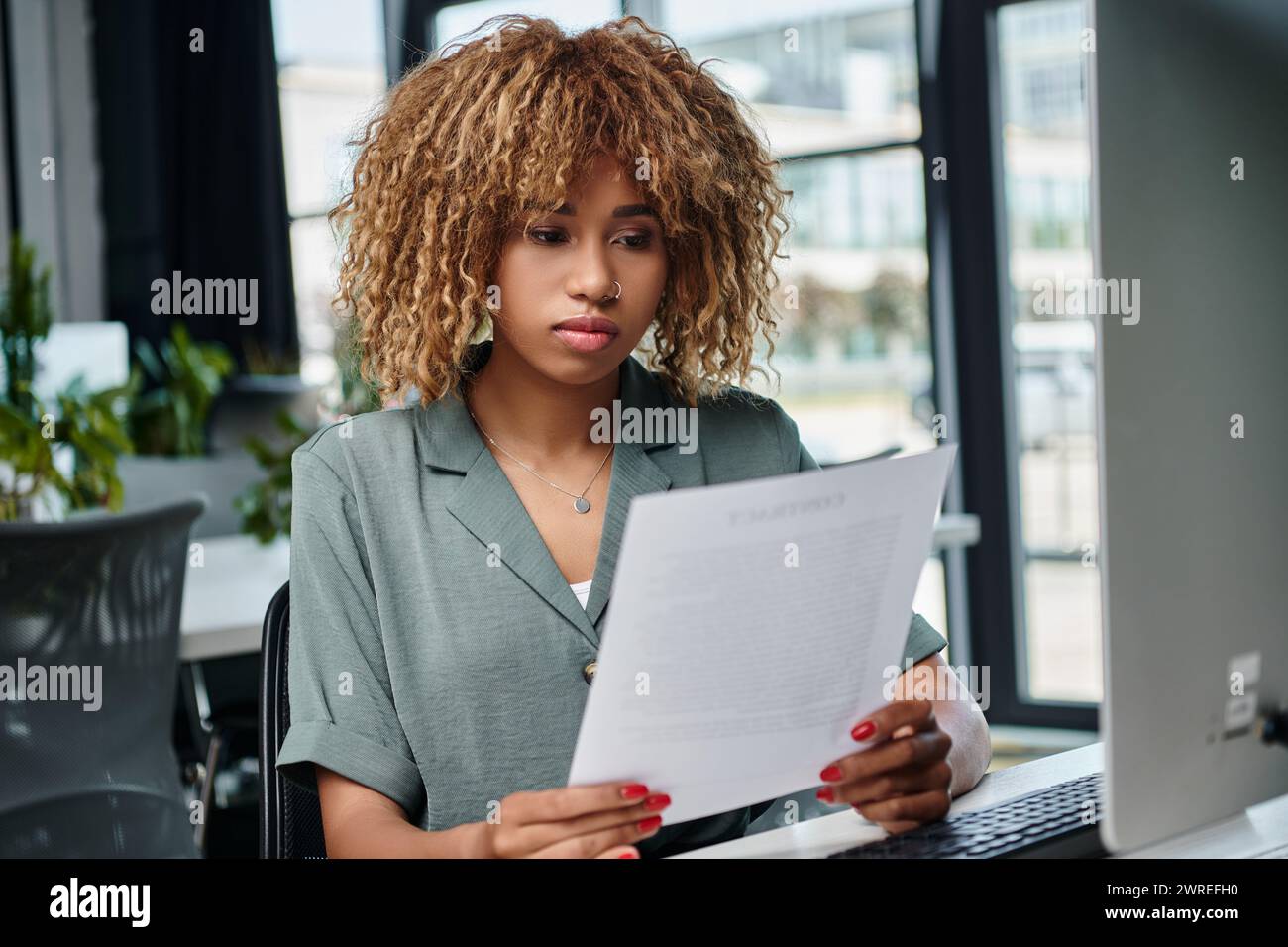 curly jeune responsable afro-américain examinant le document devant l'écran d'ordinateur dans le bureau Banque D'Images