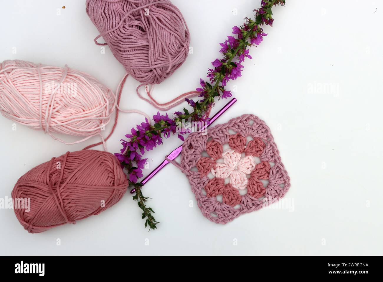 Carré Granny crocheté rose, boules de fil de coton doux de différentes nuances de couleur rose. Fond blanc avec espace de copie. Concept de crochet de ressort. Banque D'Images