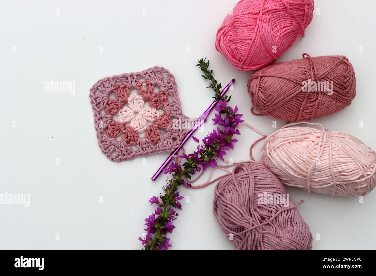 Motif au crochet, fleurs, boules de fil de coton vue de dessus photo. Carré Granny en fil organique rose doux. Motif crochet fait à la main sur fond blanc Banque D'Images