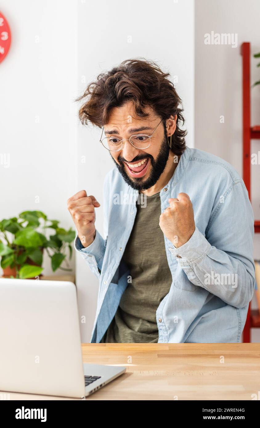 Un jeune homme excité lisant en ligne de bonnes nouvelles sur ordinateur portable à la maison Banque D'Images