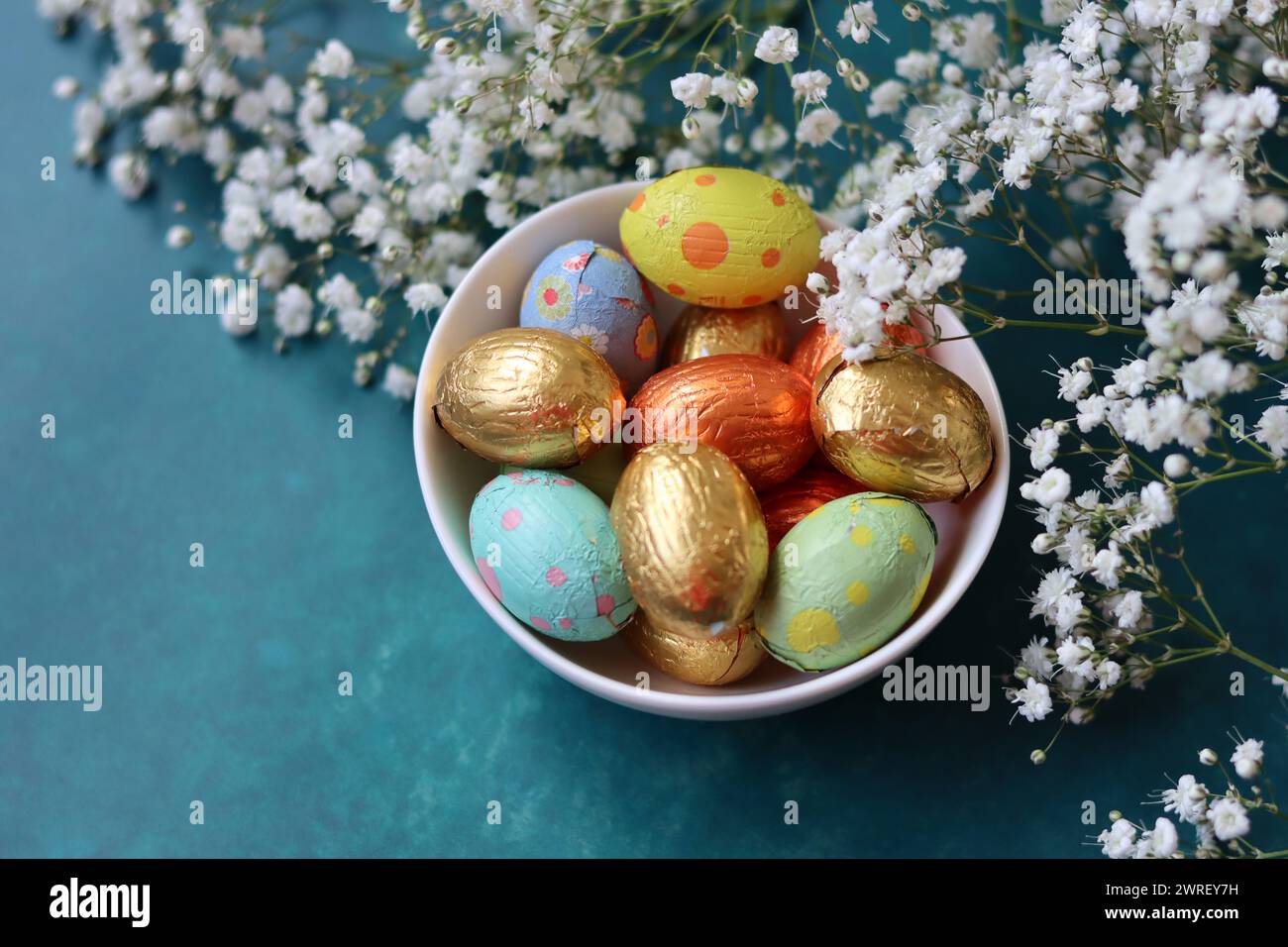 Couleurs vibrantes de bonbons de Pâques. Nature morte colorée avec des fleurs blanches de gypsophila et des œufs en chocolat. Banque D'Images