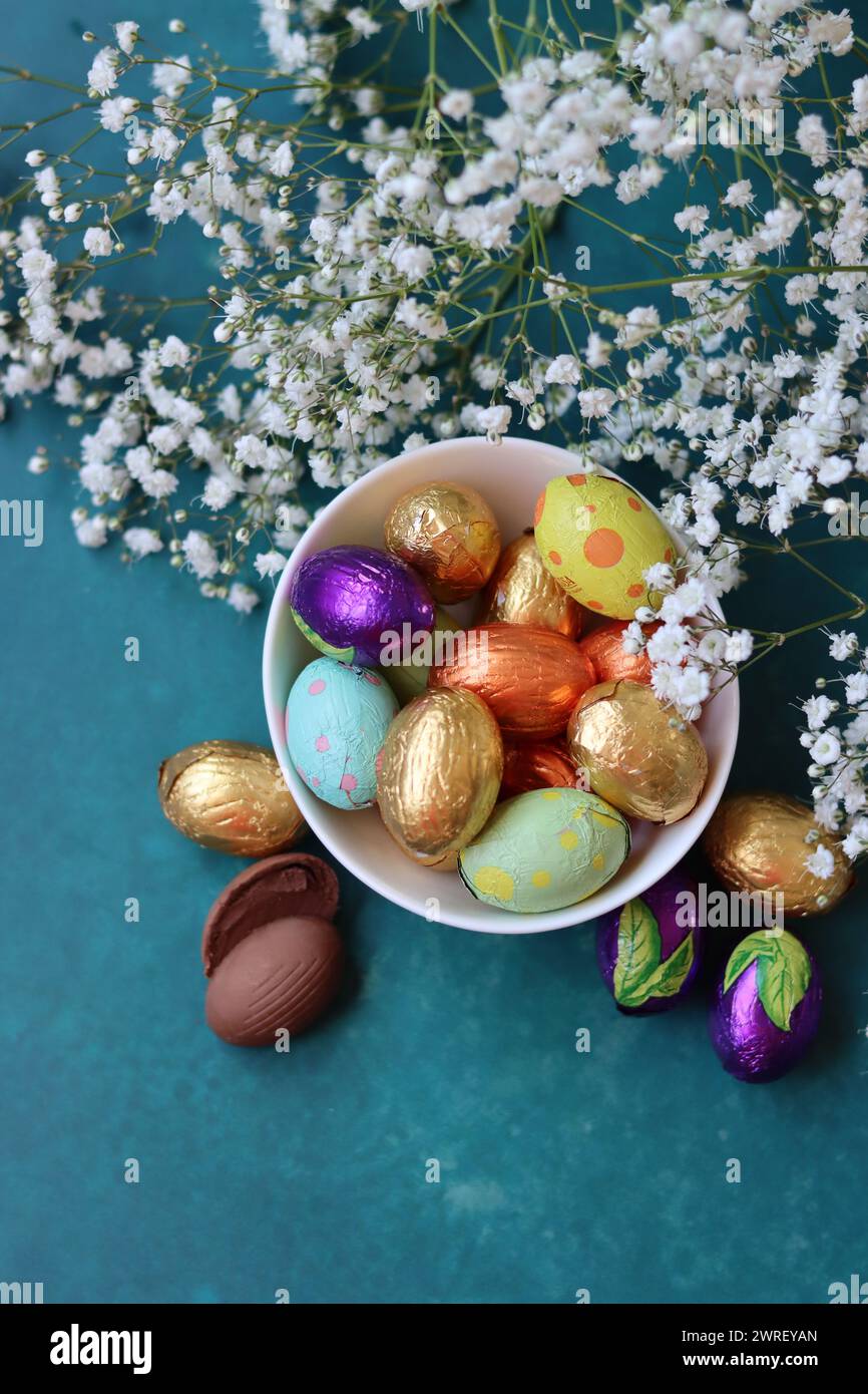 Couleurs vibrantes de bonbons de Pâques. Nature morte colorée avec des fleurs blanches de gypsophila et des œufs en chocolat. Banque D'Images