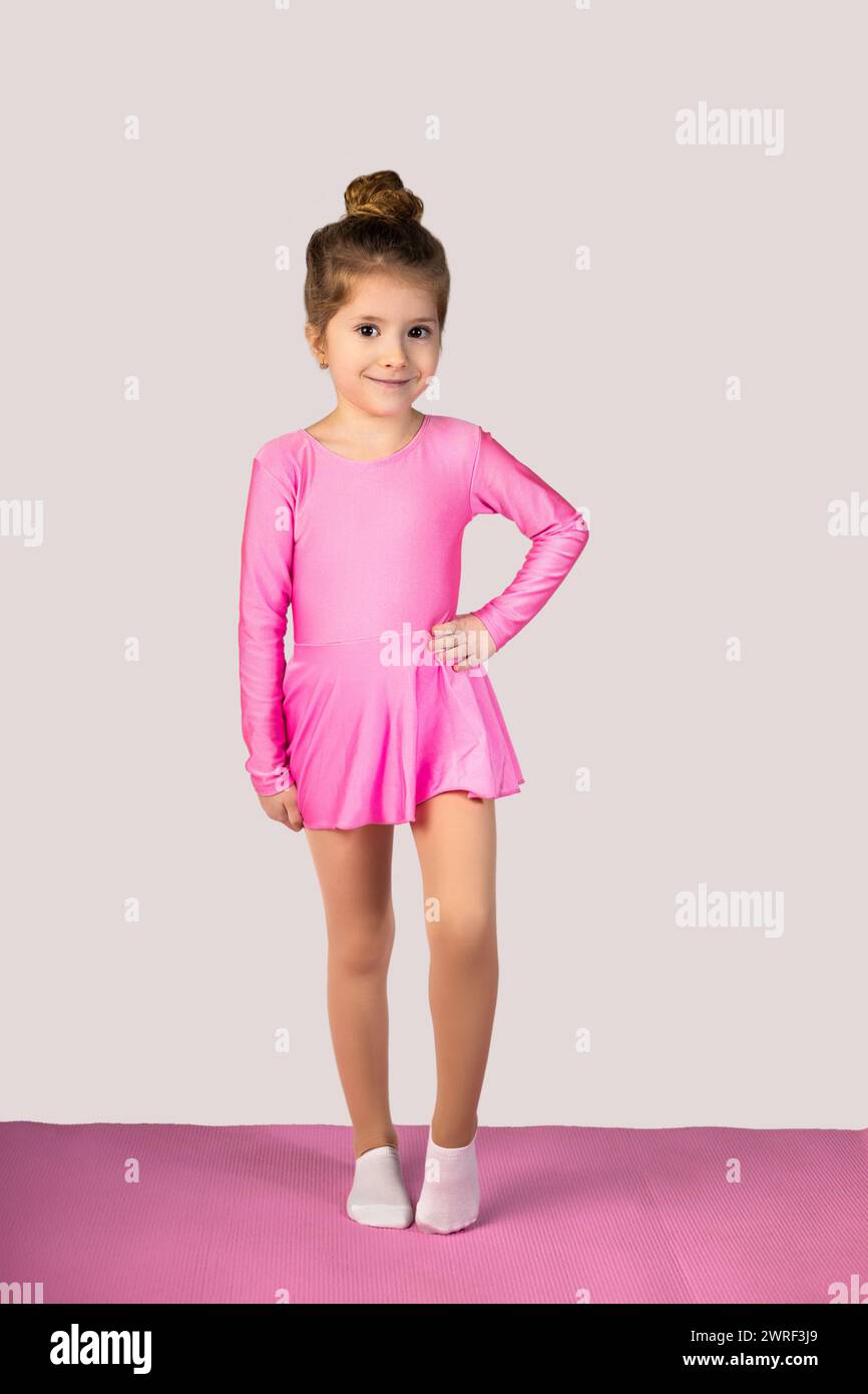 Photo pleine longueur d'une petite fille vêtue d'une robe de gym rose et avec ses cheveux dans un chignon regardant la caméra souriant et posant joliment isolé o Banque D'Images