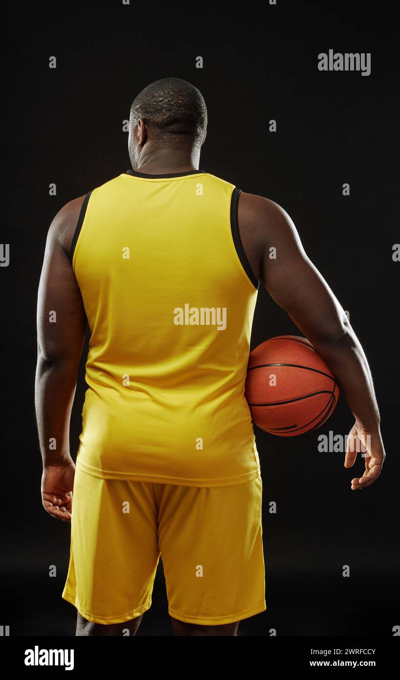 Vue arrière verticale d'un joueur de basket-ball musclé tenant le ballon tout en se tenant debout sur fond noir Banque D'Images