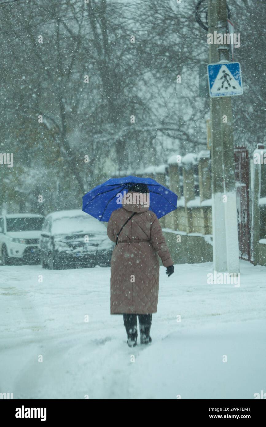 L'image d'une saison hivernale qui neige très fort et il y a des flocons masqués. Grand-mère avec un parapluie alors qu'il y a un cyclone dehors. Forte victoire Banque D'Images