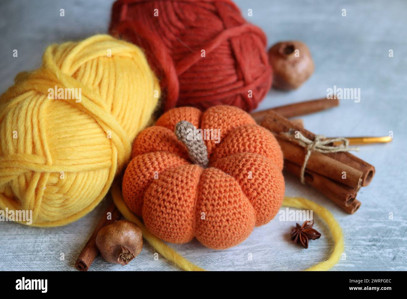 Tricoter des natures mortes d'automne. Aiguilles à tricoter, fils de laine, anis, cannelle, citrouille crochetée sur fond gris clair avec espace pour le texte. Banque D'Images