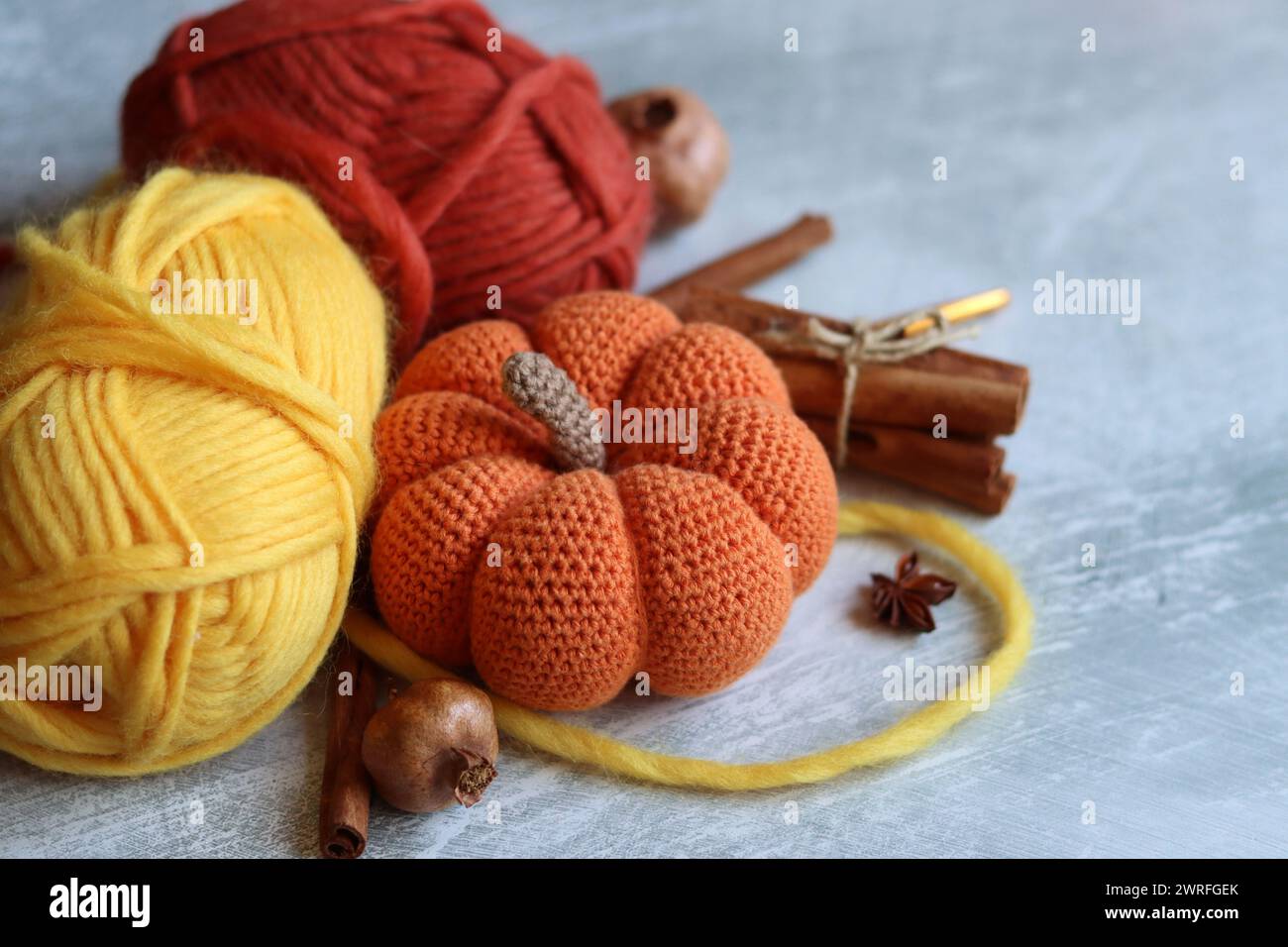 Tricoter des natures mortes d'automne. Aiguilles à tricoter, fils de laine, anis, cannelle, citrouille crochetée sur des idées cadeaux de jour de Thanksgiving gris clair. Banque D'Images