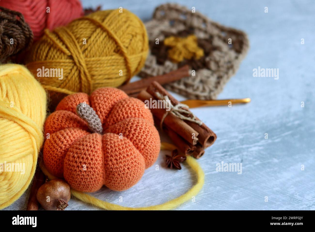 Tricoter des natures mortes d'automne. Aiguilles à tricoter, fils de laine, anis, cannelle, citrouille crochetée sur fond gris clair avec espace pour le texte. Banque D'Images