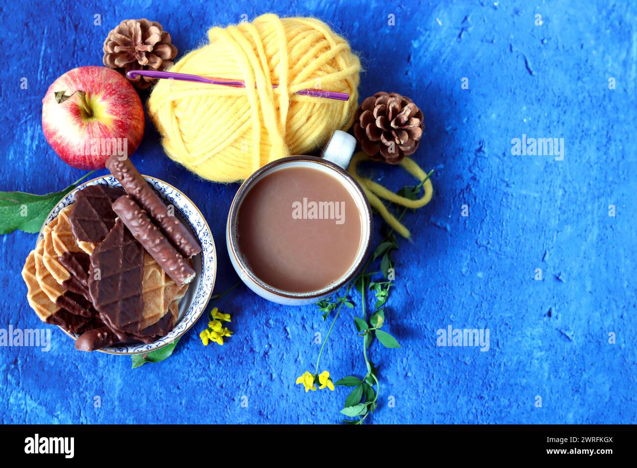 Tasse de café avec du lait, des gaufres, des pommes et du chocolat et des boules de fil sur un fond bleu avec espace de copie. Concept d'automne confortable. Banque D'Images