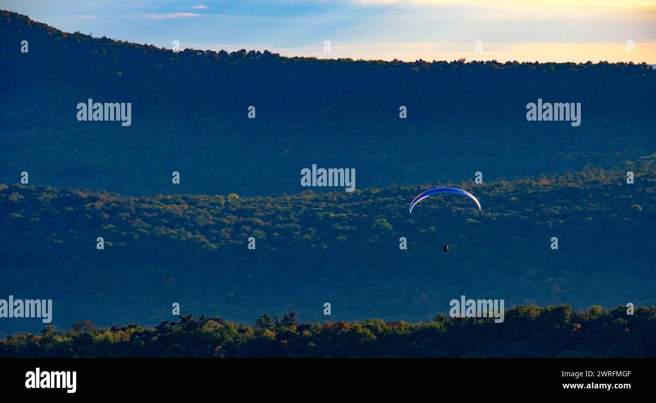 Parapente survolant une chaîne de montagnes boisée au crépuscule avec le gradient du ciel en arrière-plan. Banque D'Images
