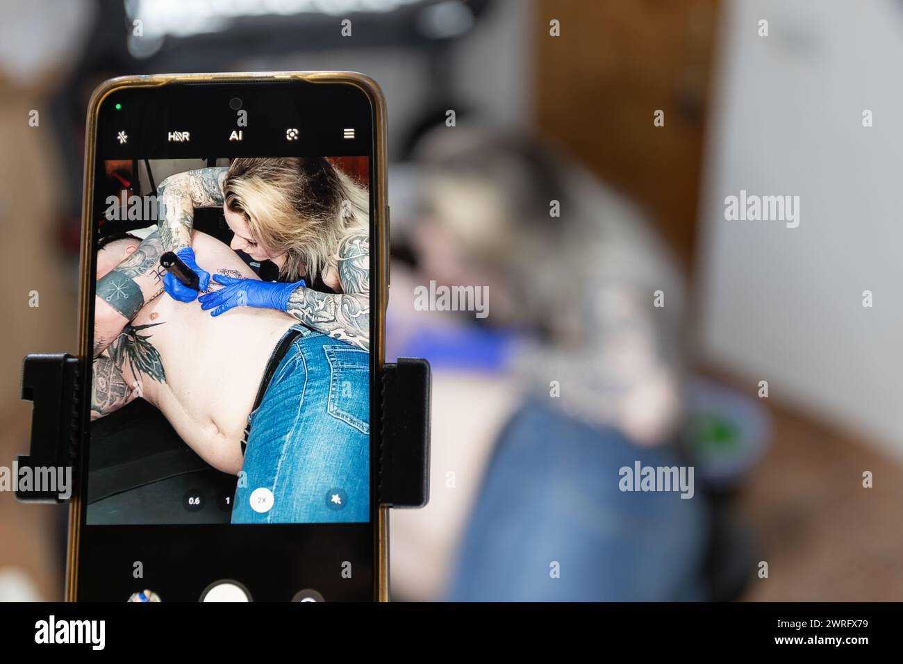 Image photo horizontale à travers un smartphone capturant le travail ciblé d'un tatoueur comme ils encrent un dessin sur la peau. Concept business, compris Banque D'Images