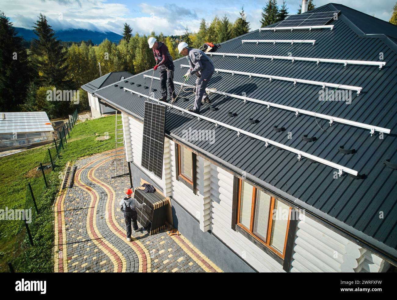 Travailleurs professionnels soulevant le panneau solaire sur un toit de maison. Deux techniciens homme transportant le module solaire photovoltaïque. Concept d'énergie alternative et renouvelable. Banque D'Images