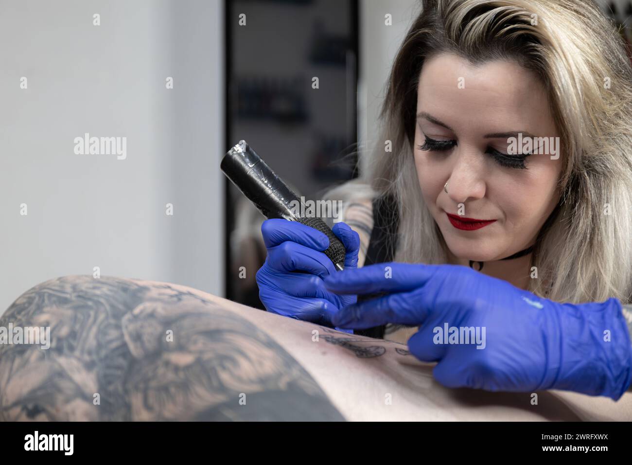 Photo horizontale une artiste tatoueuse méticuleuse applique de l'encre avec précision, son attention captée par l'évolution de l'œuvre d'art sur la peau. Copier l'espace. Concept bu Banque D'Images