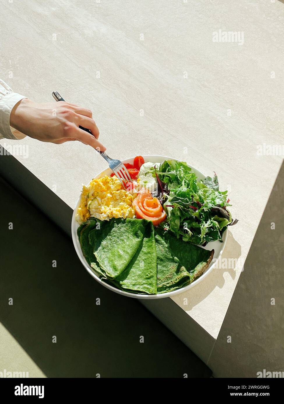 Vue aérienne d'une femme mangeant des crêpes aux épinards, des œufs brouillés, du saumon, des tomates et de la laitue Banque D'Images