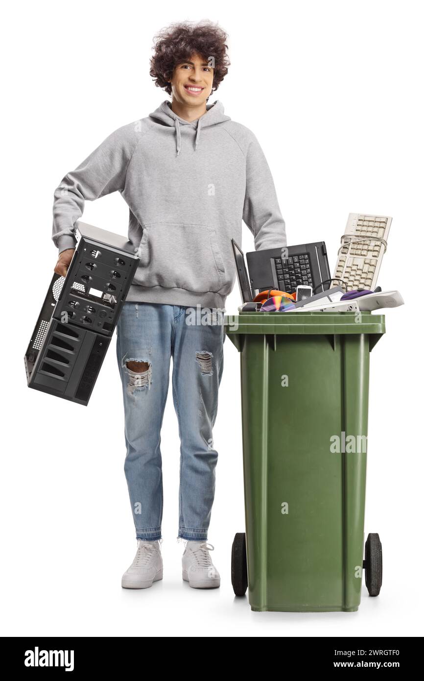 Jeune homme jetant un vieil ordinateur et debout à côté d'une poubelle avec des déchets électroniques isolés sur fond blanc Banque D'Images