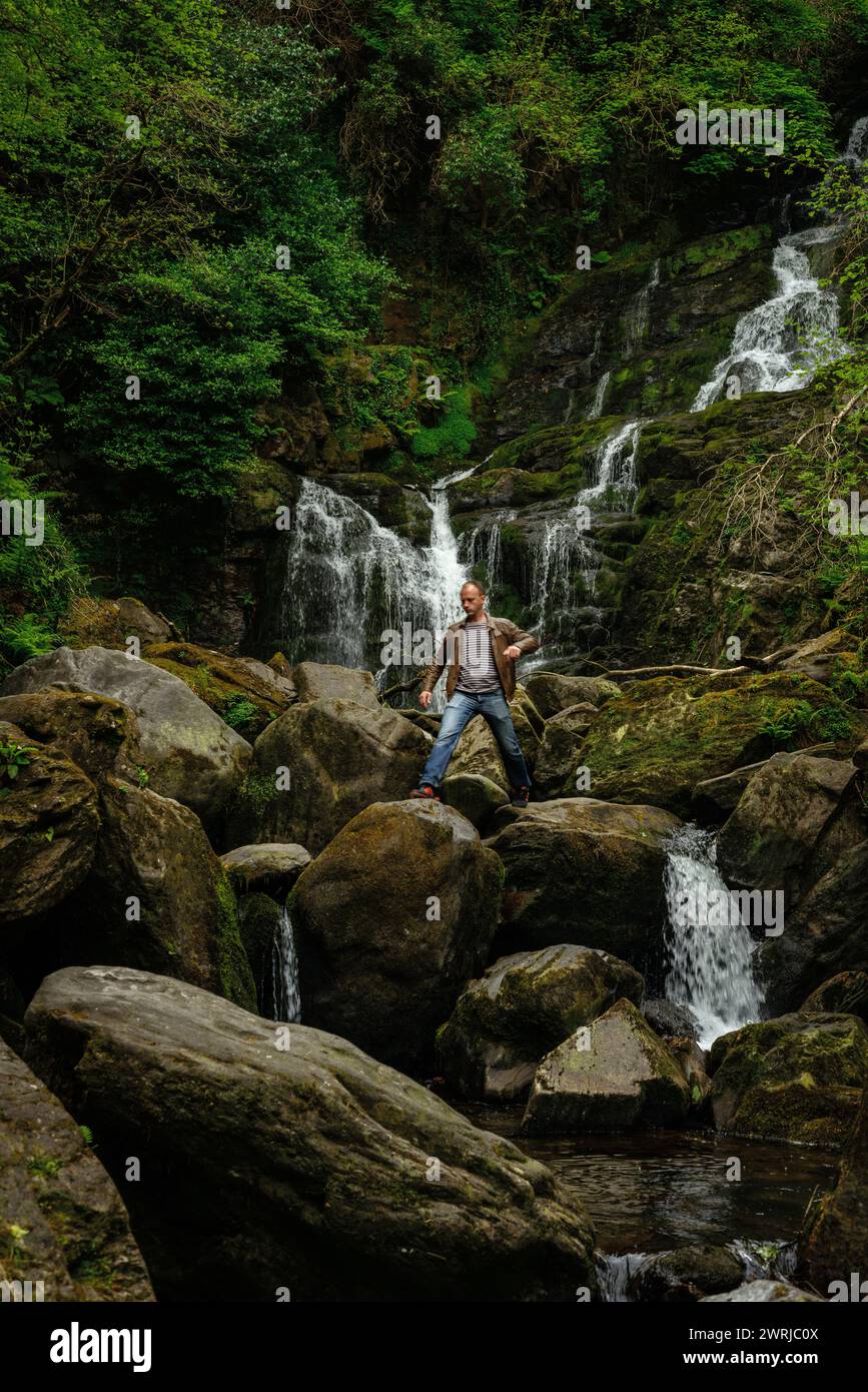Touriste masculin posant pour la photo sur des rochers à la cascade de Torc dans le parc national de Killarney, comté de Kerry, Irlande Banque D'Images