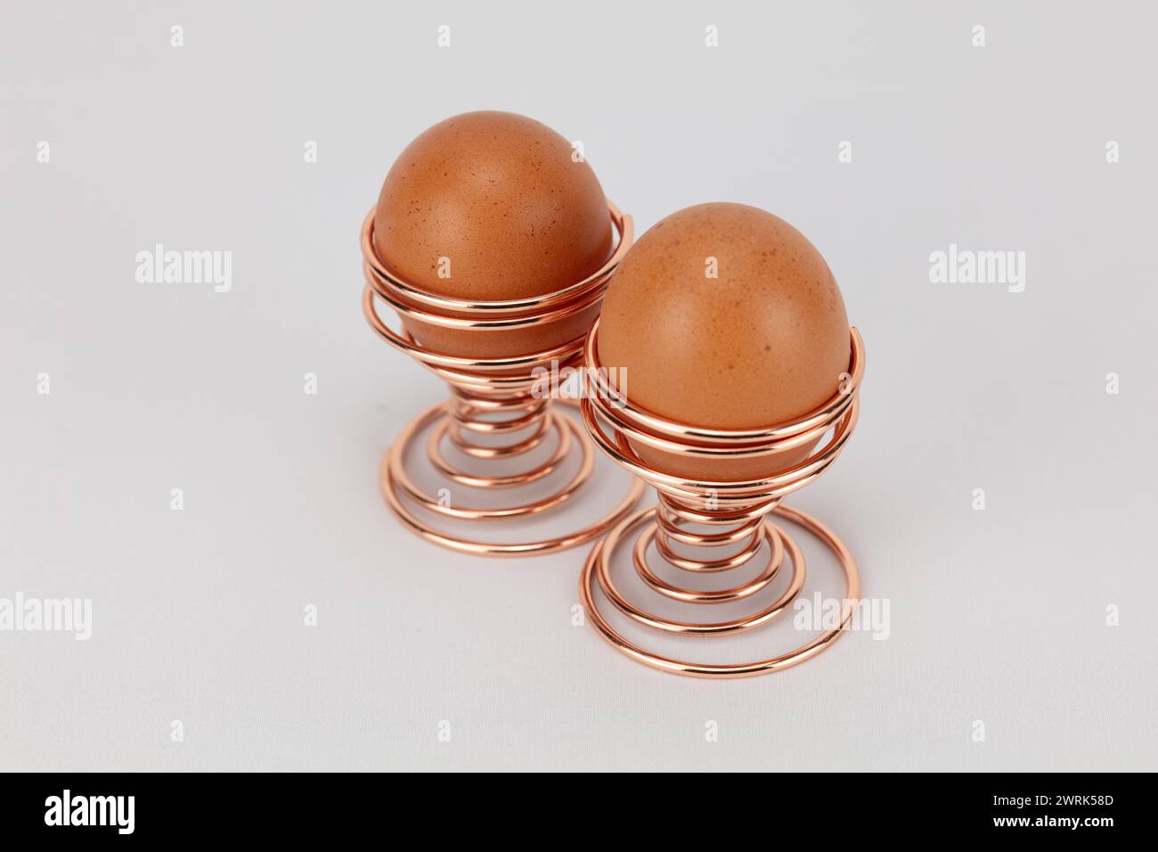 deux grands œufs fermiers en or rose ou en cuivre spiralé coquetiers sur un fond pâle modifiable Banque D'Images
