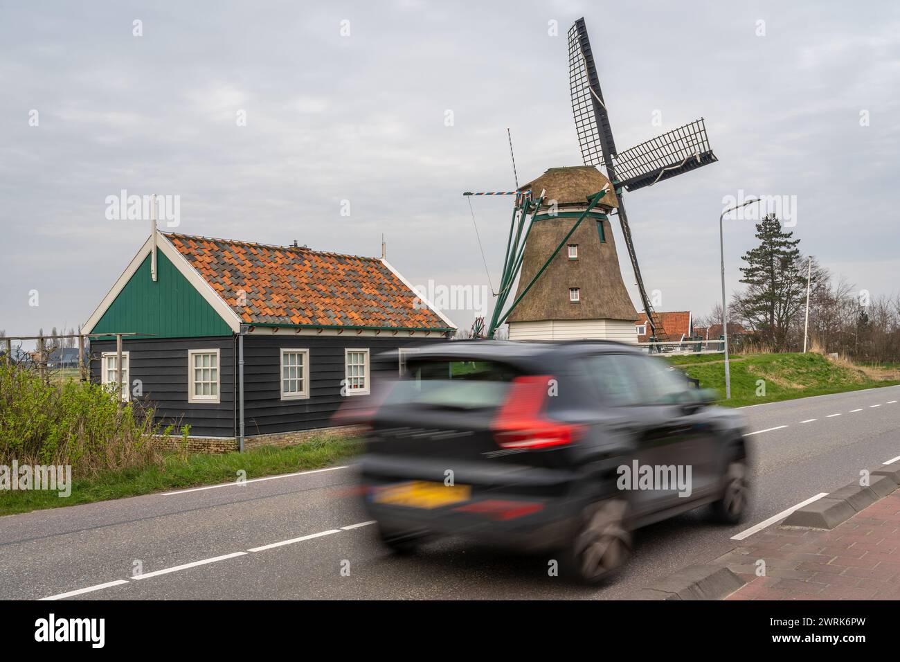 La voiture passe devant le moulin à vent hollandais traditionnel. Déplacements et circulation aux pays-Bas. Flou de mouvement intentionnel. Banque D'Images