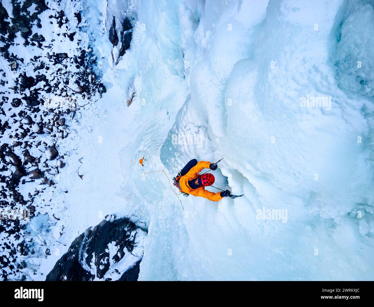 Vue aérienne drone de l'athlète en veste orange escalade de glace à grande cascade gelée dans la gorge Barskoon la vallée de montagne au Kirghizistan Banque D'Images