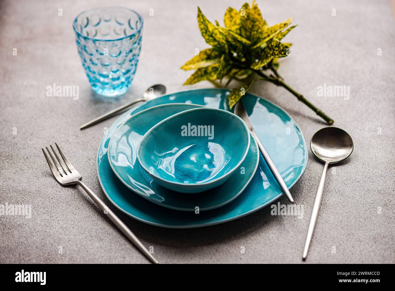 Vaisselle turquoise éclatante avec verre et couverts assortis sur une surface grise texturée. Banque D'Images