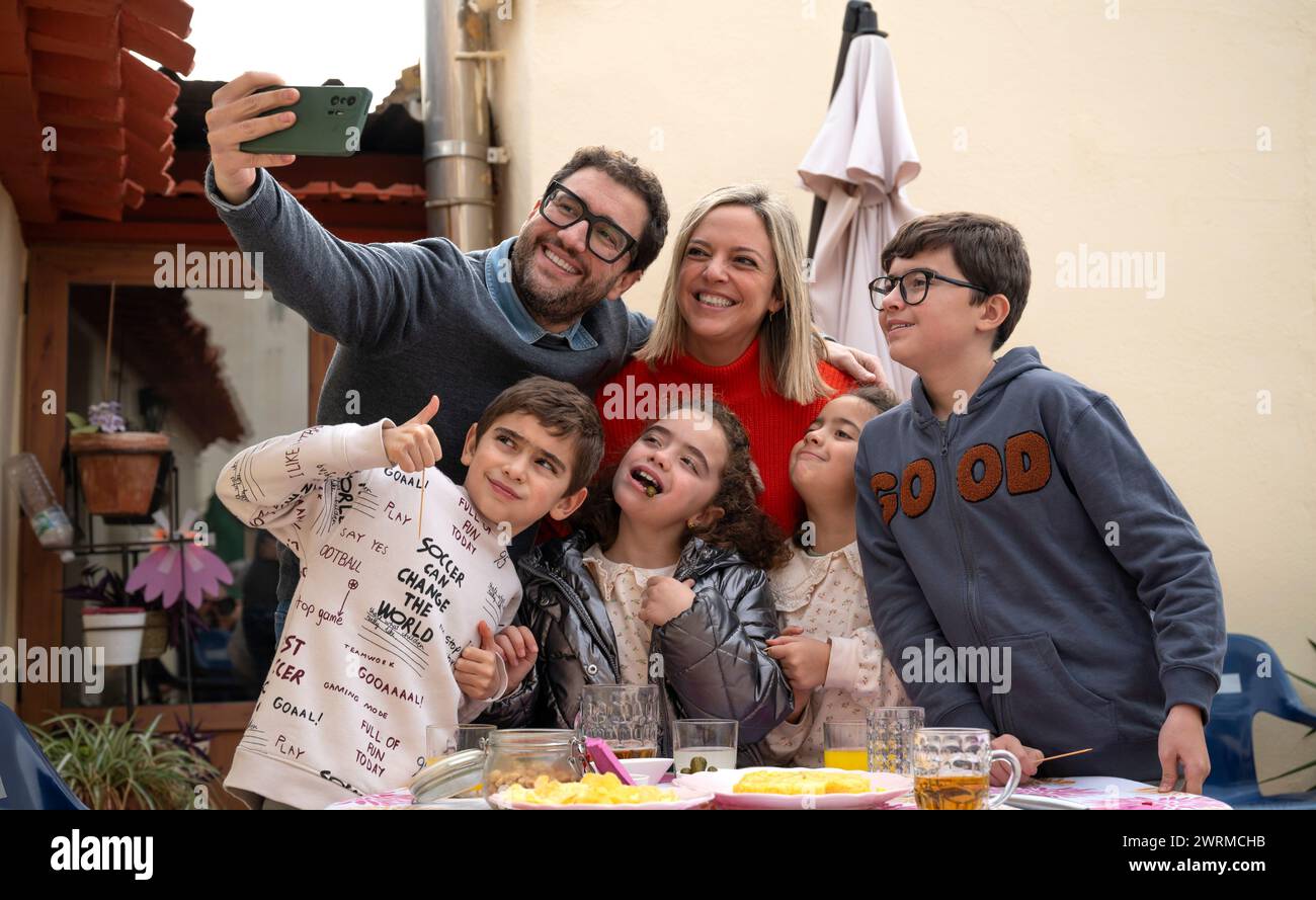 Une famille heureuse de six sourires pour un selfie autour d'une table avec de la nourriture lors d'une réunion de famille en plein air. Banque D'Images