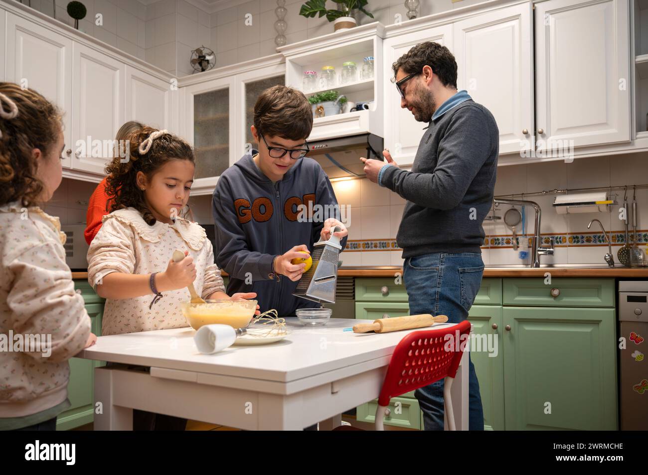 Une scène familiale réconfortante où les enfants et un adulte s'engagent dans des activités culinaires dans une cuisine accueillante, ajoutant à la chaleur et à la joie d'une réunion de famille. Banque D'Images