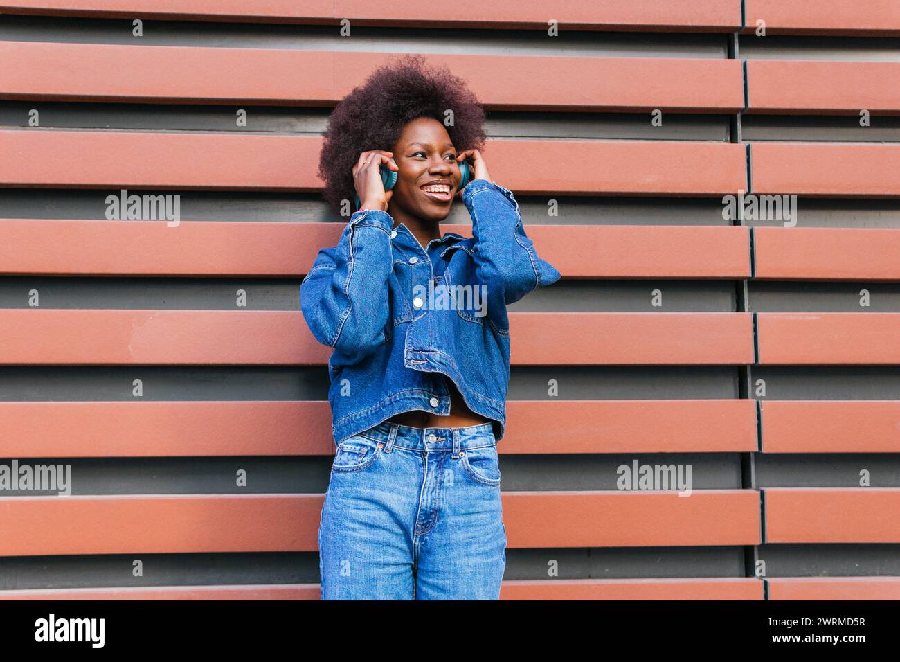 Une femme rayonnante apprécie ses airs préférés, habillée de la tête aux pieds en denim classique sur fond géométrique en terre cuite Banque D'Images
