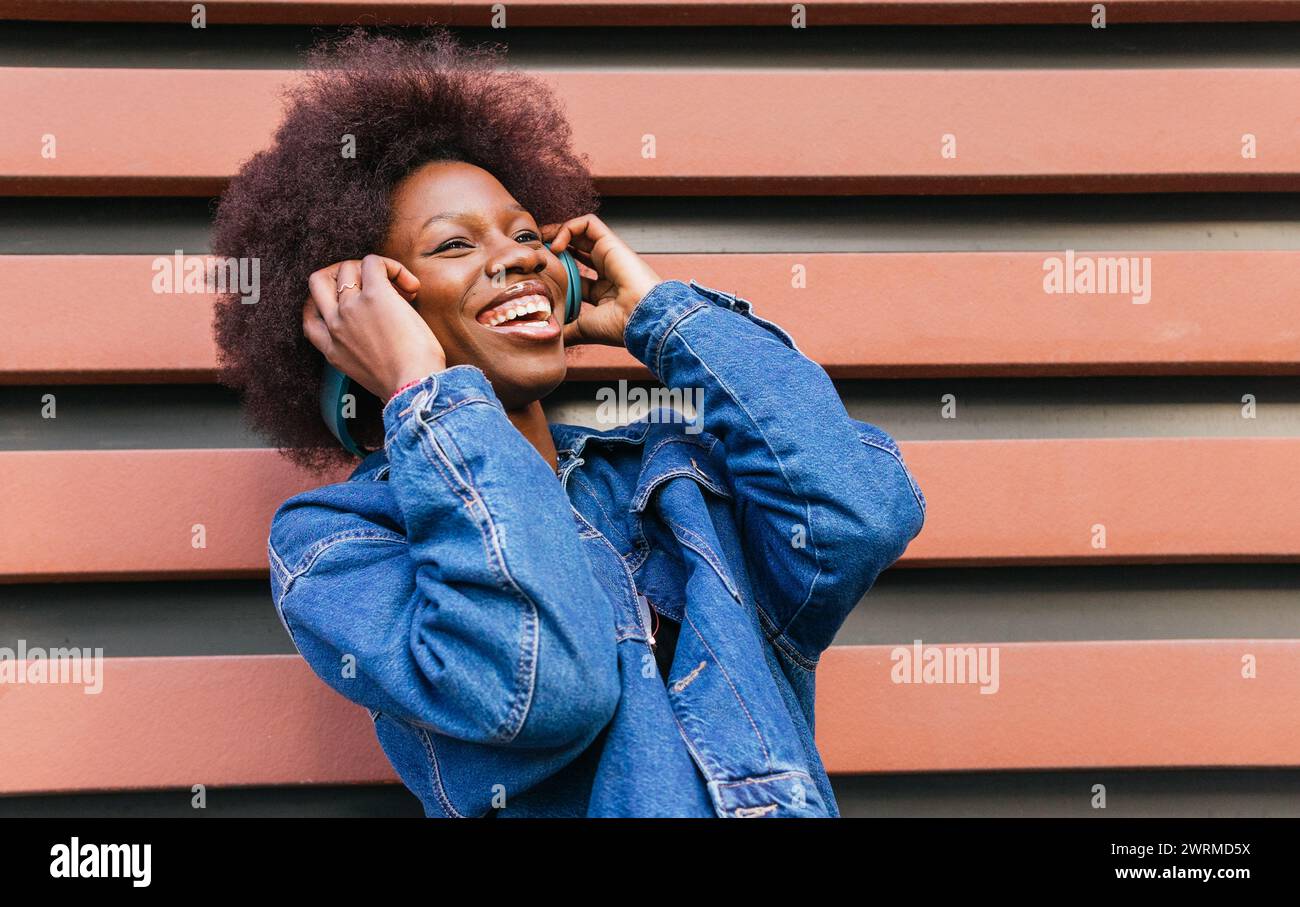 Une jeune femme exubérante au sourire radieux profite de la mélodie dans son casque, créant un moment de bonheur urbain Banque D'Images
