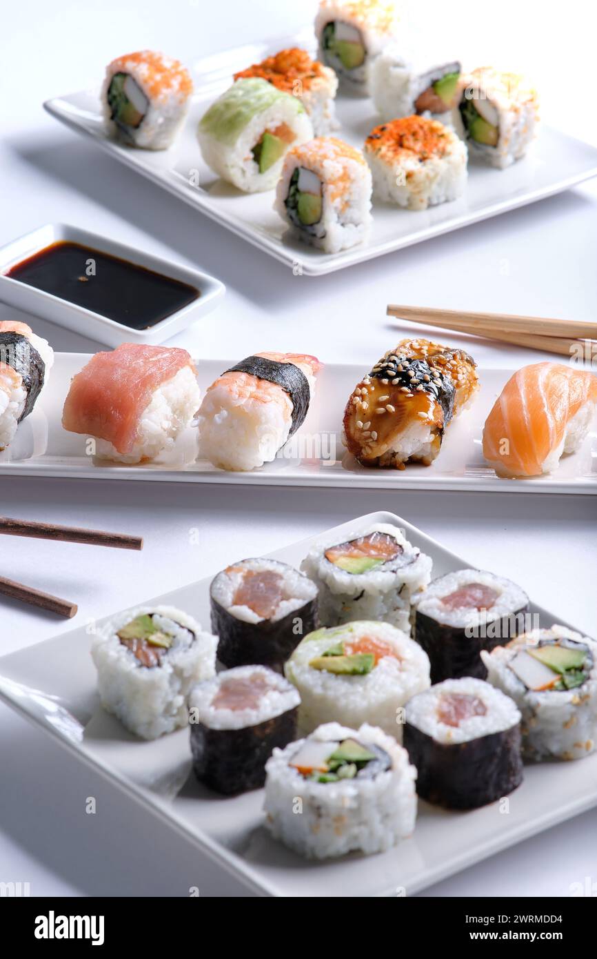 Un appétissant assortiment de rouleaux de sushi soigneusement disposés sur deux assiettes blanches, accompagnés de sauce soja et de baguettes. Banque D'Images