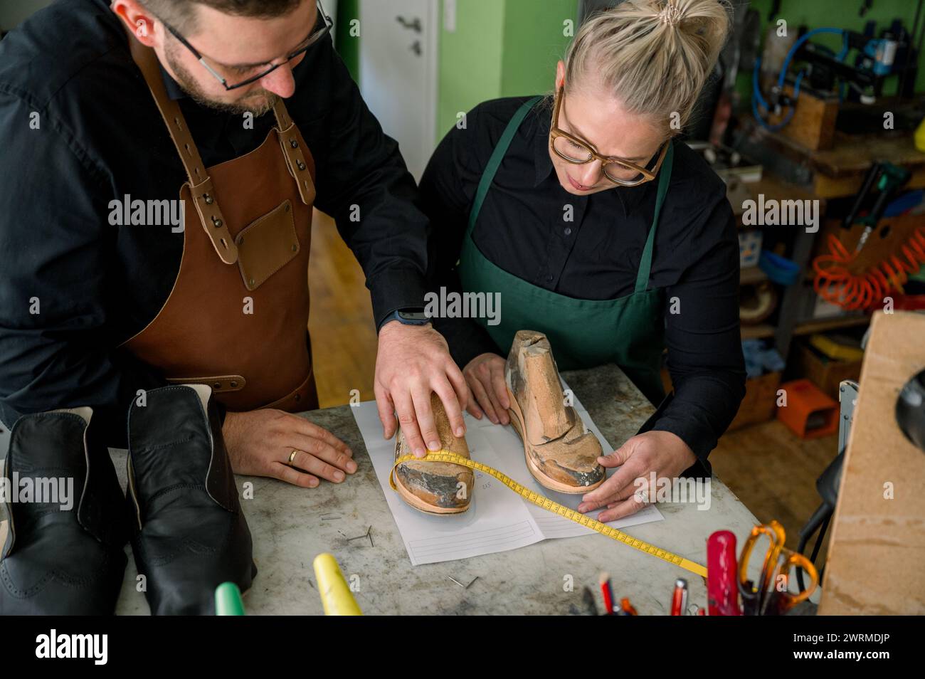 Deux artisans mesurent une chaussure dans un atelier de cordonnerie autrichienne traditionnelle chaleureusement éclairé. Banque D'Images